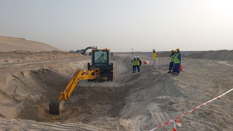 Backhoe loader excavating a trench while site staff look on