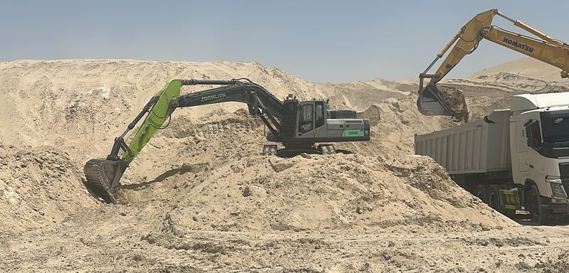 Two excavators working on a sand stockpile, one loading a dump truck