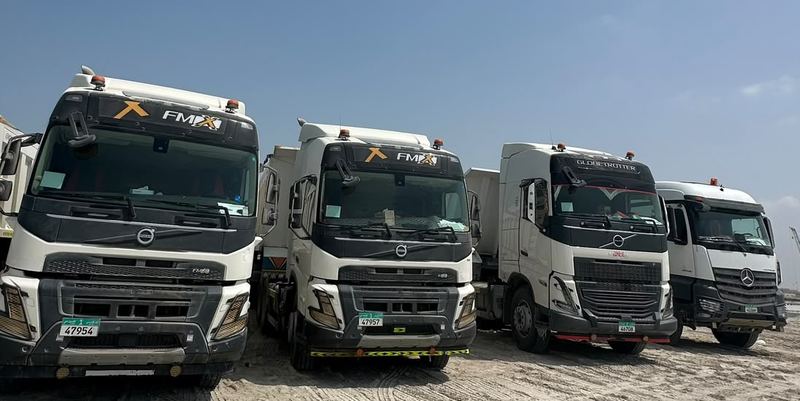 Row of company trucks with tipper trailers parked on site