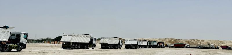 Long line of tipper trucks crossing a sand site